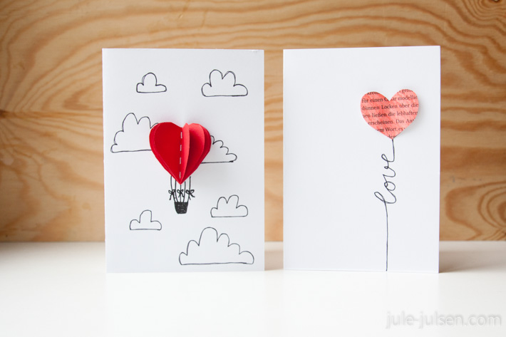 zwei Valentinstagskarten aus Papier: links = heissluftballon in Herzform in den Wolken, rechts = Luftballon in Herzform mit Schnur, die das Wort 