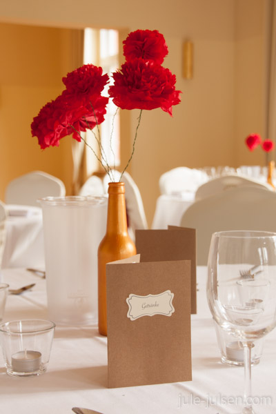 Dekoration des Dinnertisches mit in gold bemalten Flaschen und roten Papierblumen 