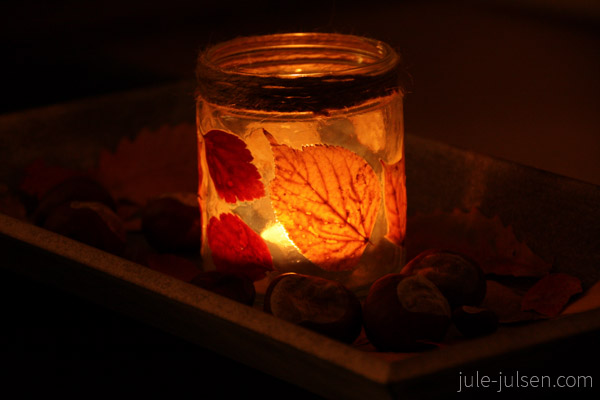 altes Marmeladenglas beklebt mit Herbstblättern und Teelicht im Dunkeln