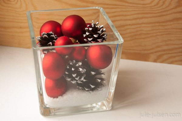 eckige Glasschale mit roten Weihnachtskugeln und weiss bemalten Kienaepfeln