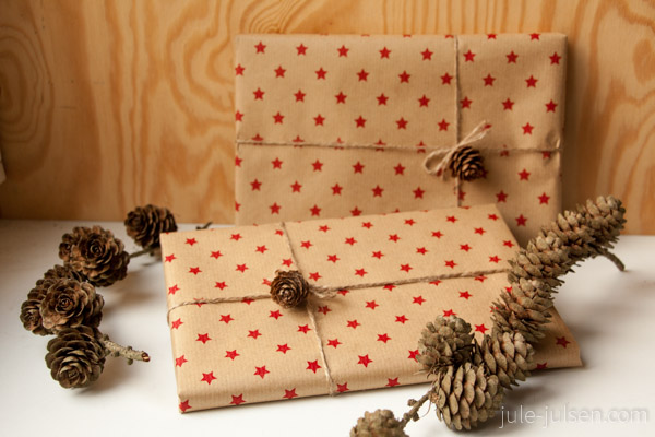 geschenkverpackung aus braunem packpapier mit roten sternen und lerchenzapfen als dekoration