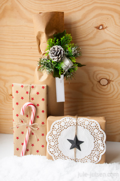 links: geschenkverpackung aus braunem packpapier mit roten sternen, mitte: flaschenverpackung aus braunem packpapier mit dekto aus kienapfel und tannengruen, rechts: geschenkverpackung aus braunem packpapier verziert mit weißem tortenpapier