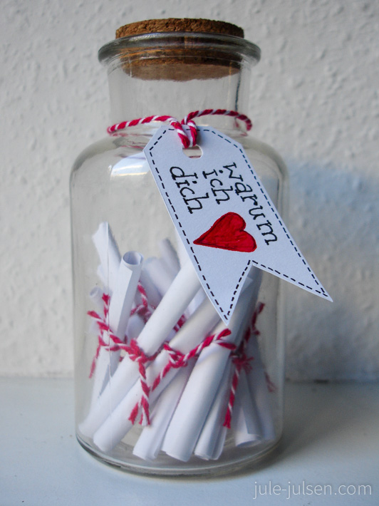 Glasflasche mit zusammengerollten Liebesbotschaften darin und angehängtem Etikett mit der Aufschrift 