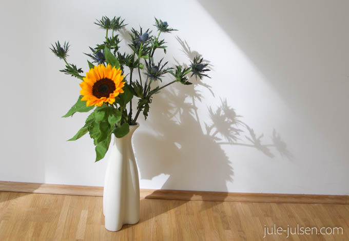 Blumenstrauss mit Disteln und einer Sonnenblume in schlichter weißer Vase